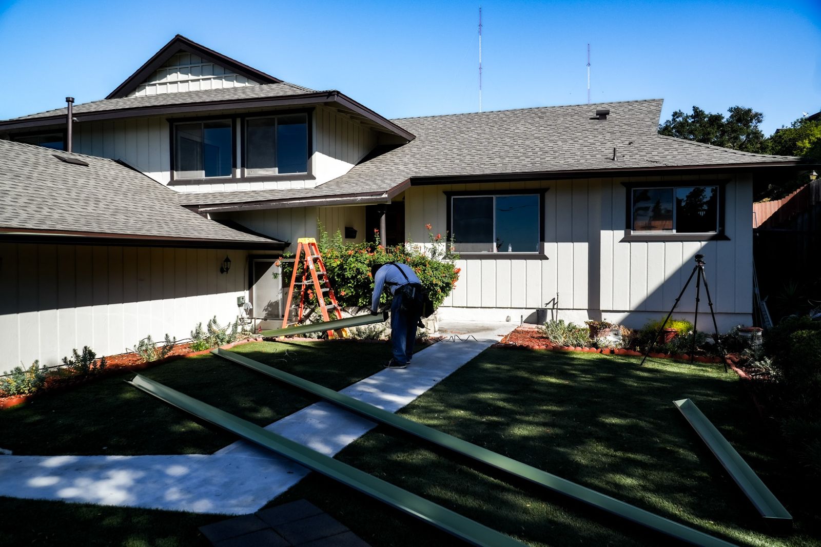 Coastline installer at work on a two-story Los Angeles home with fresh gutter sections staged on the lawn.